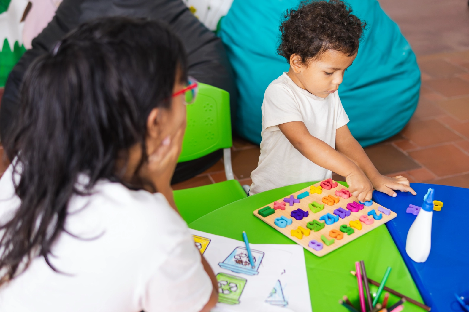 Child playing with puzzle, adult watching nearby.