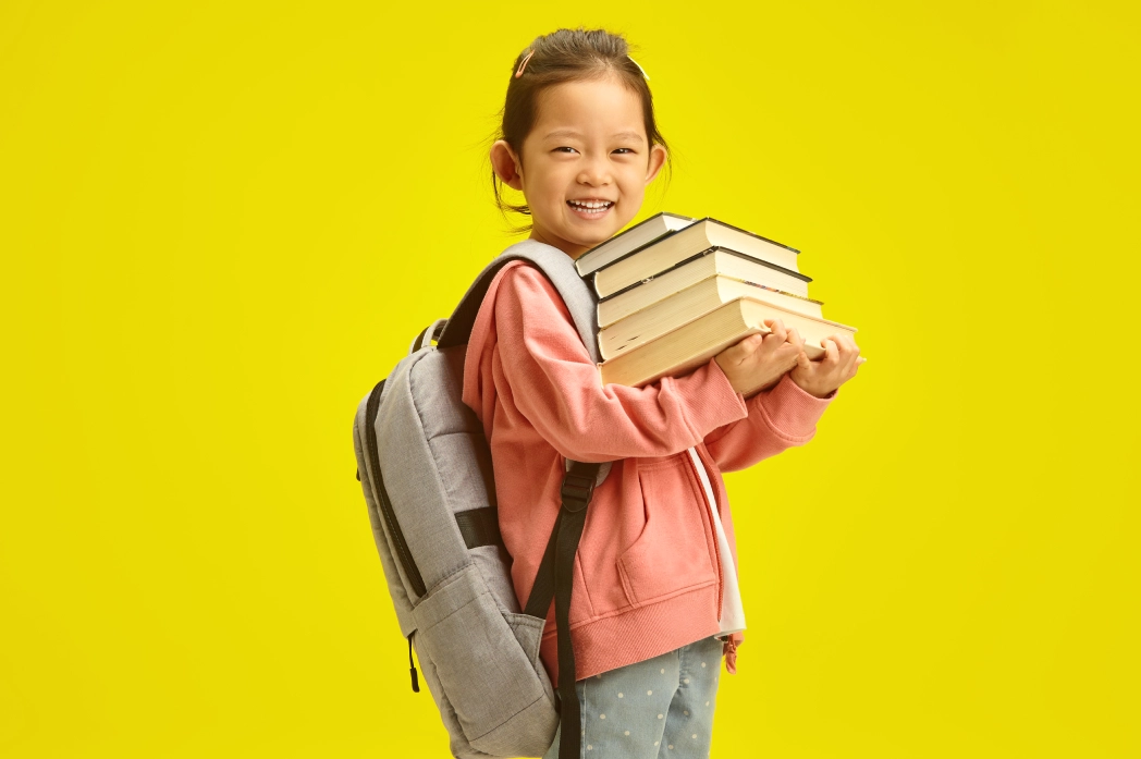 GettyImages-2201772644 (1) (1) Child smiling with backpack and books.