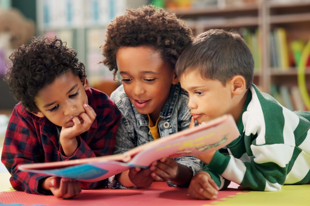 GettyImages-2201772644 (1) (2) Children reading a book together on floor.