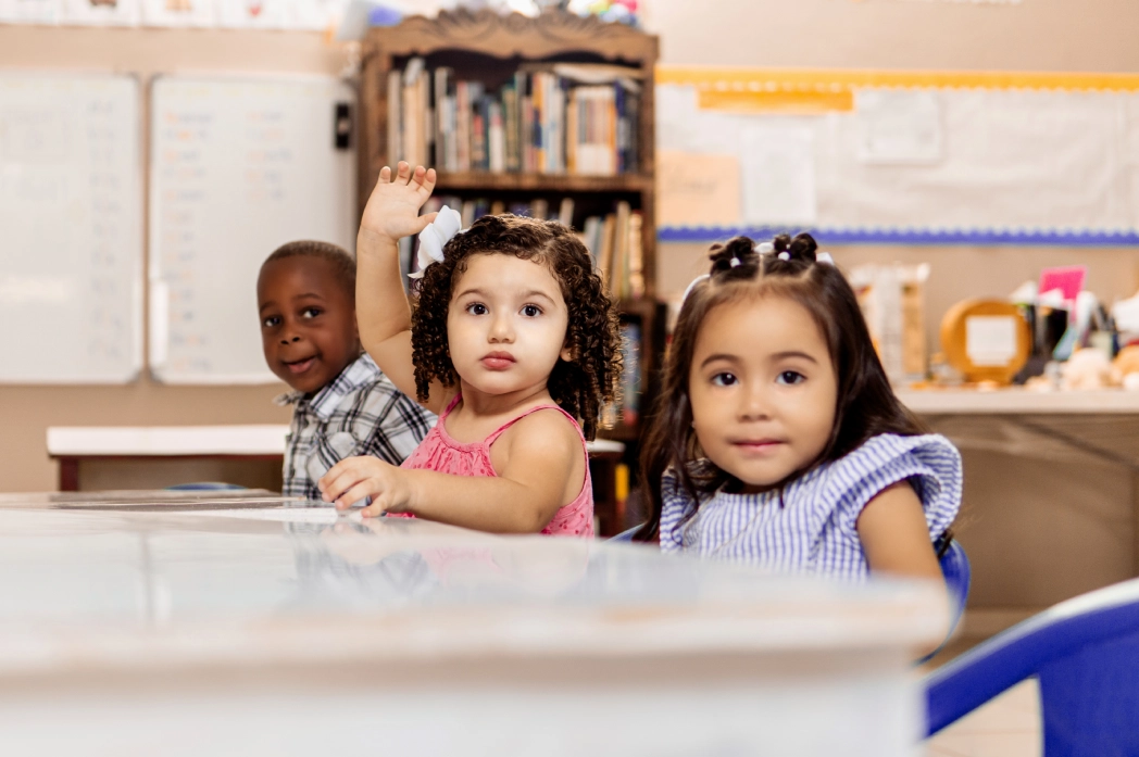 Children seated in classroom, one raising hand.